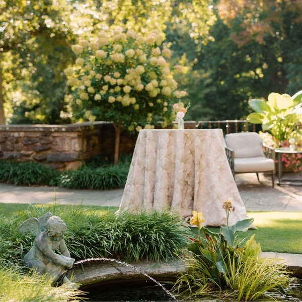 a table with a white cloth and a fountain in the middle of a garden