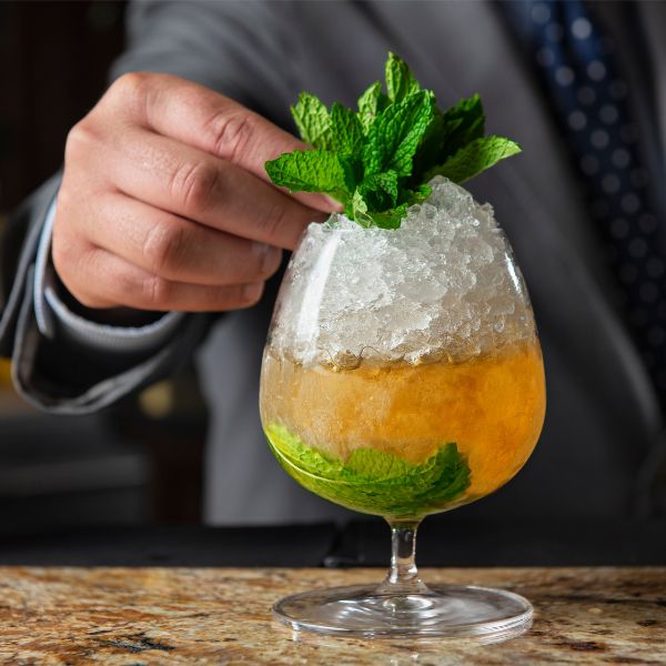 a hand holding a drink with a leaf of mint in a glass