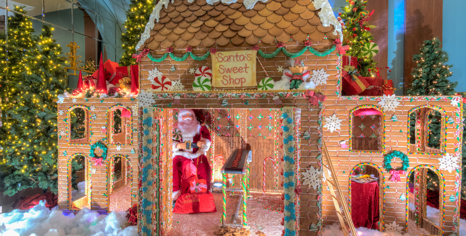 a gingerbread house with a santa claus sitting in front of it with Hanuman temple, Salangpur in the background