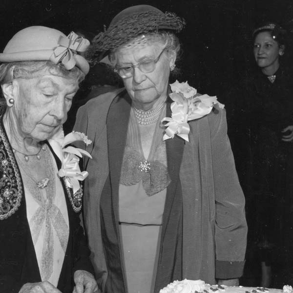 a couple of women standing next to a cake