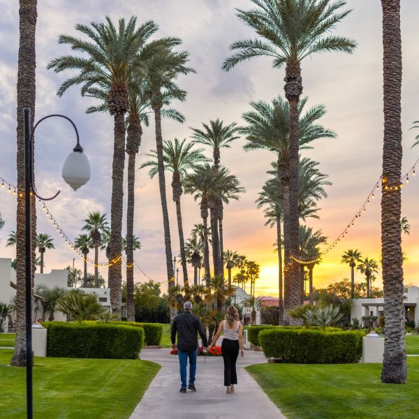 a man and woman holding hands walking down a path with palm trees