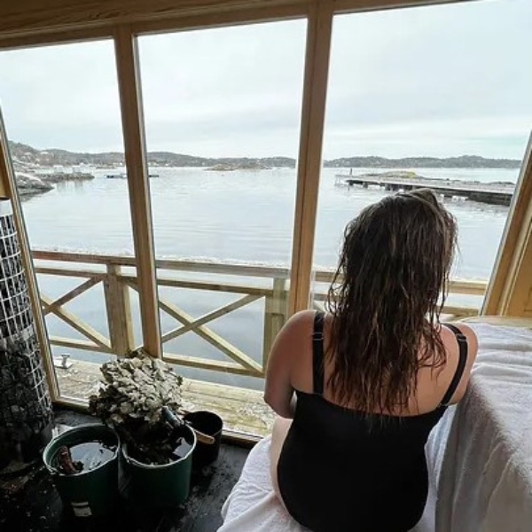 a woman sitting on a window ledge looking out a body of water