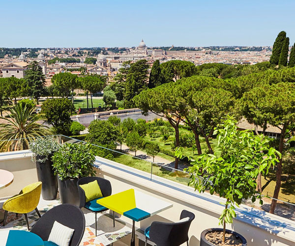 a rooftop patio with trees and chairs and a city in the background