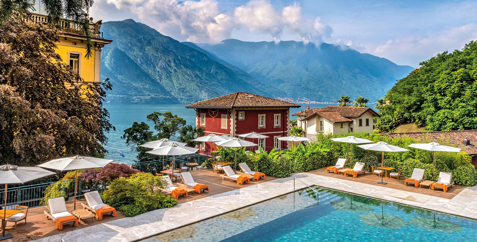 a pool with chairs and umbrellas by a house and mountains