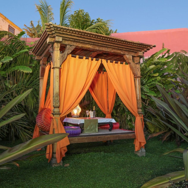 a wooden structure with orange curtains and a table in the middle of a garden