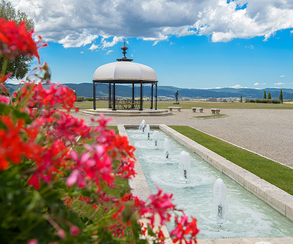 a fountain in a park with a gazebo and flowers