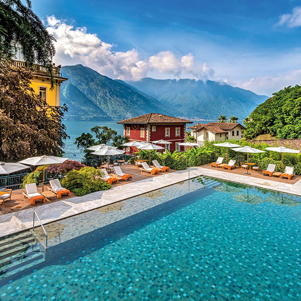 a pool with chairs and umbrellas by a building and mountains