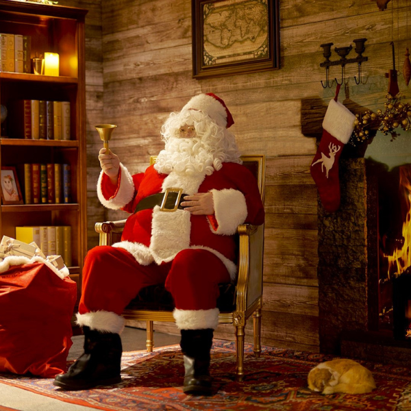 a man in a santa garment sitting in a chair by a fireplace
