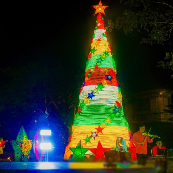 a group of people playing instruments in front of a christmas tree