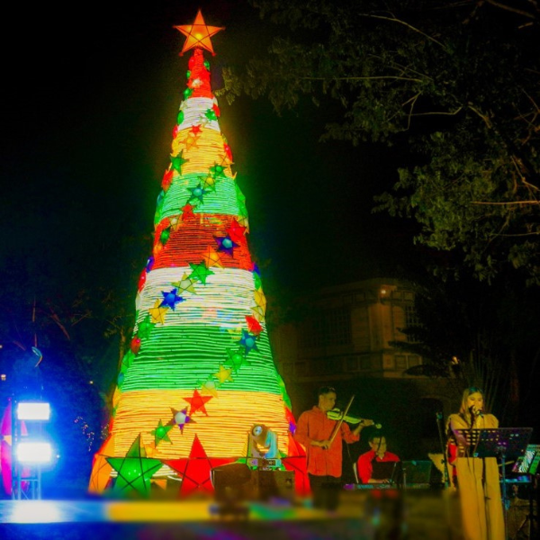 a group of people playing instruments in front of a christmas tree