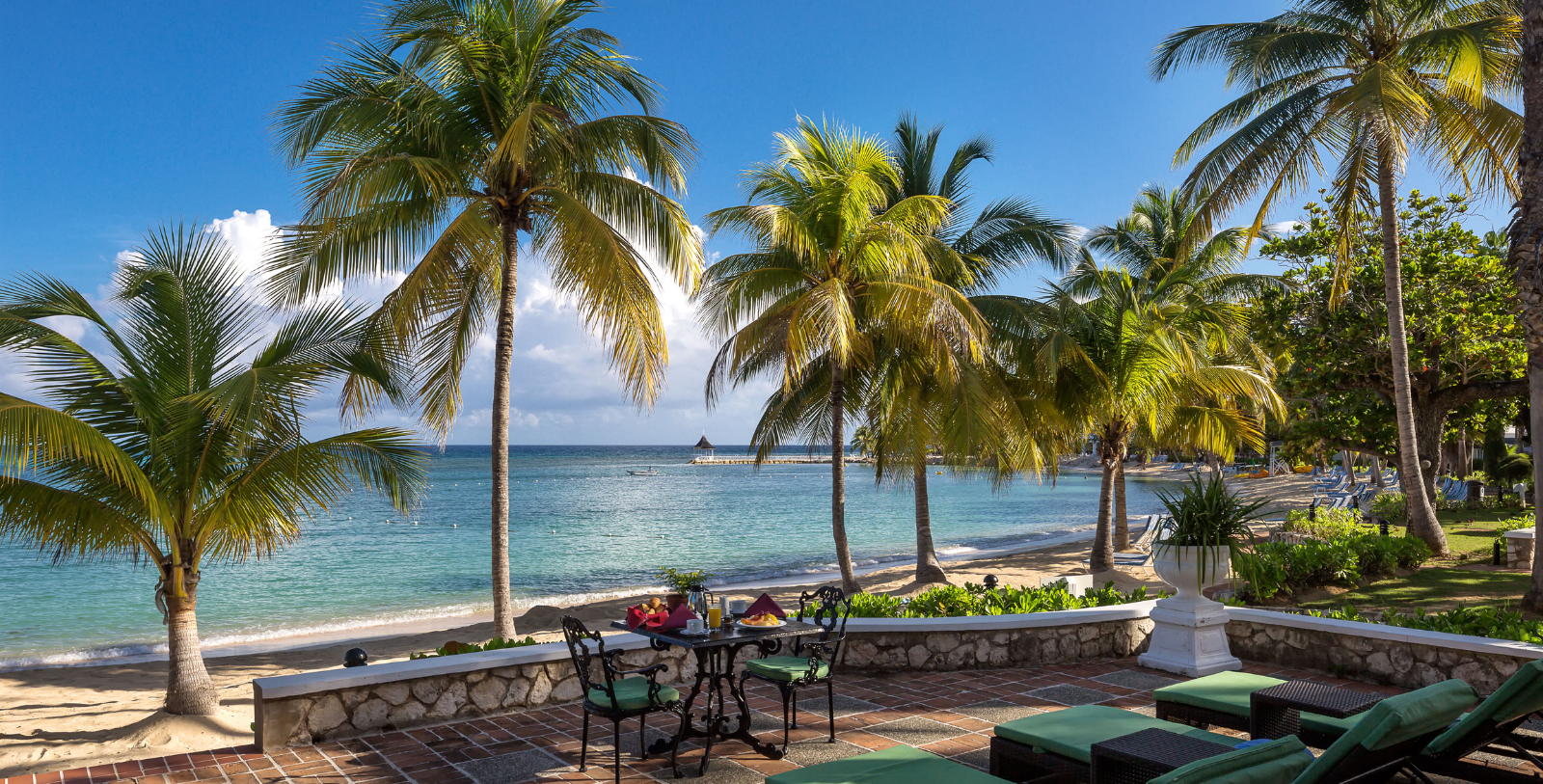 a table and chairs on a patio with palm trees and a body of water