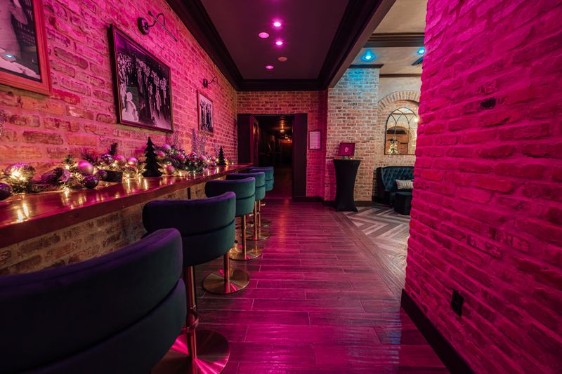 a long bar with chairs and a table in a room with pink lights