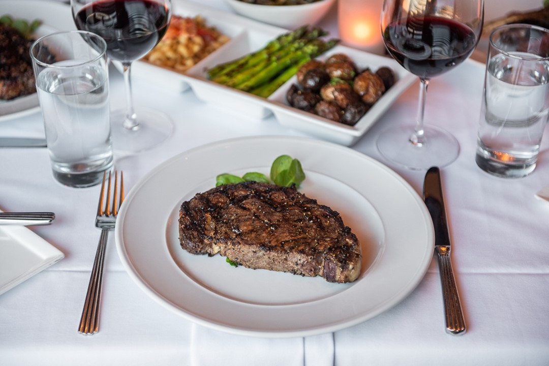 a steak on a plate with a plate of food and wine