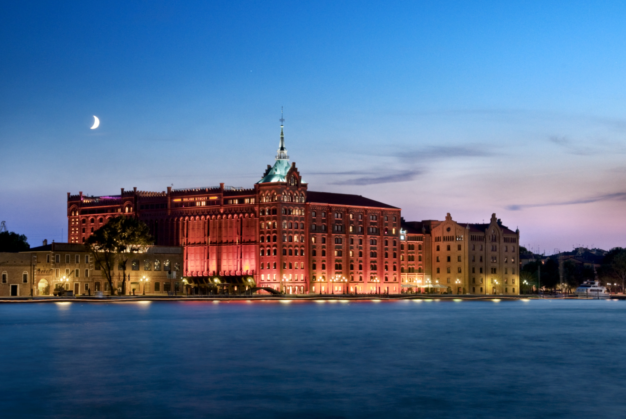 a large building with lights on the side of the water