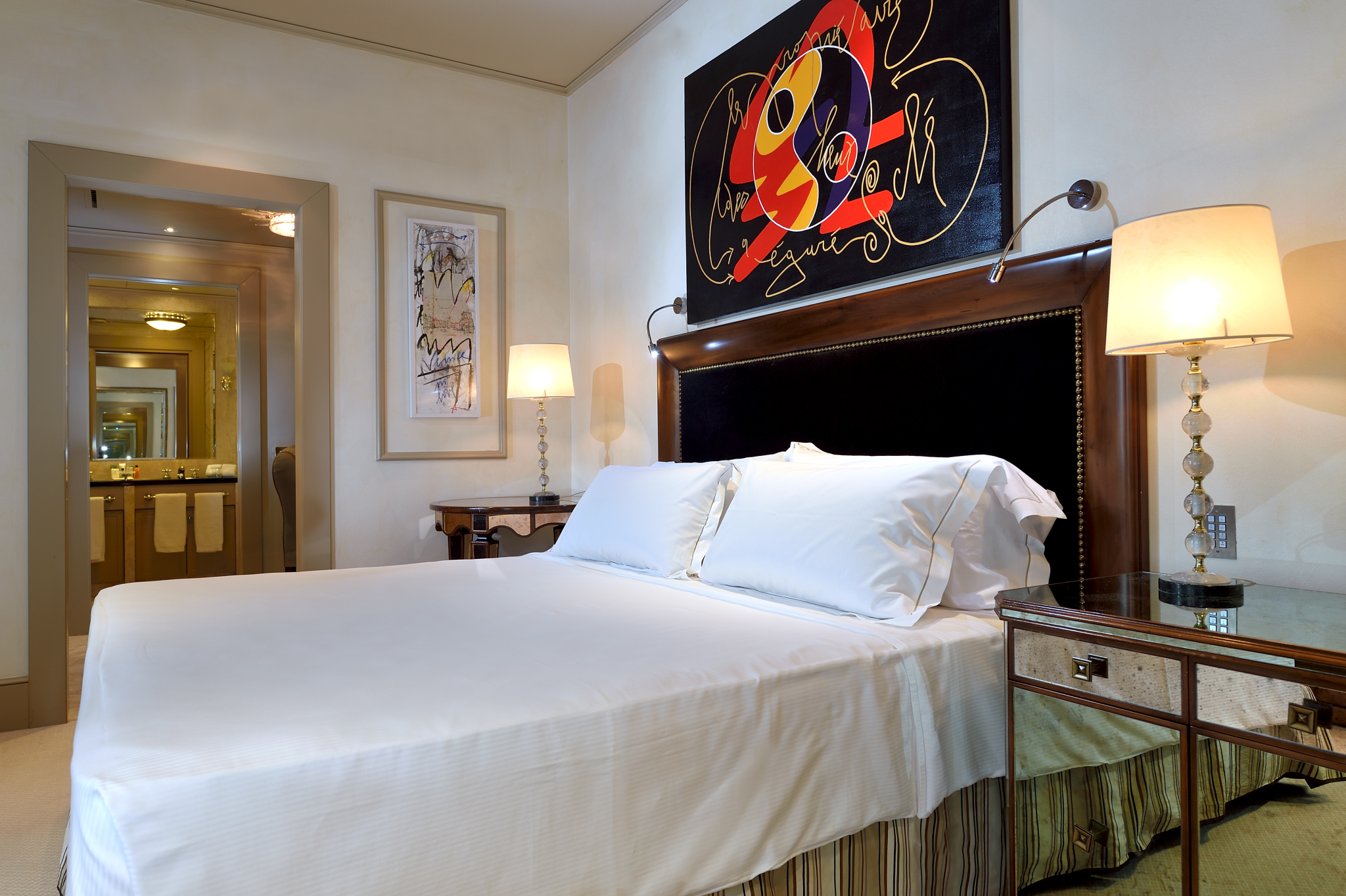 a bed with white sheets and a painting above it