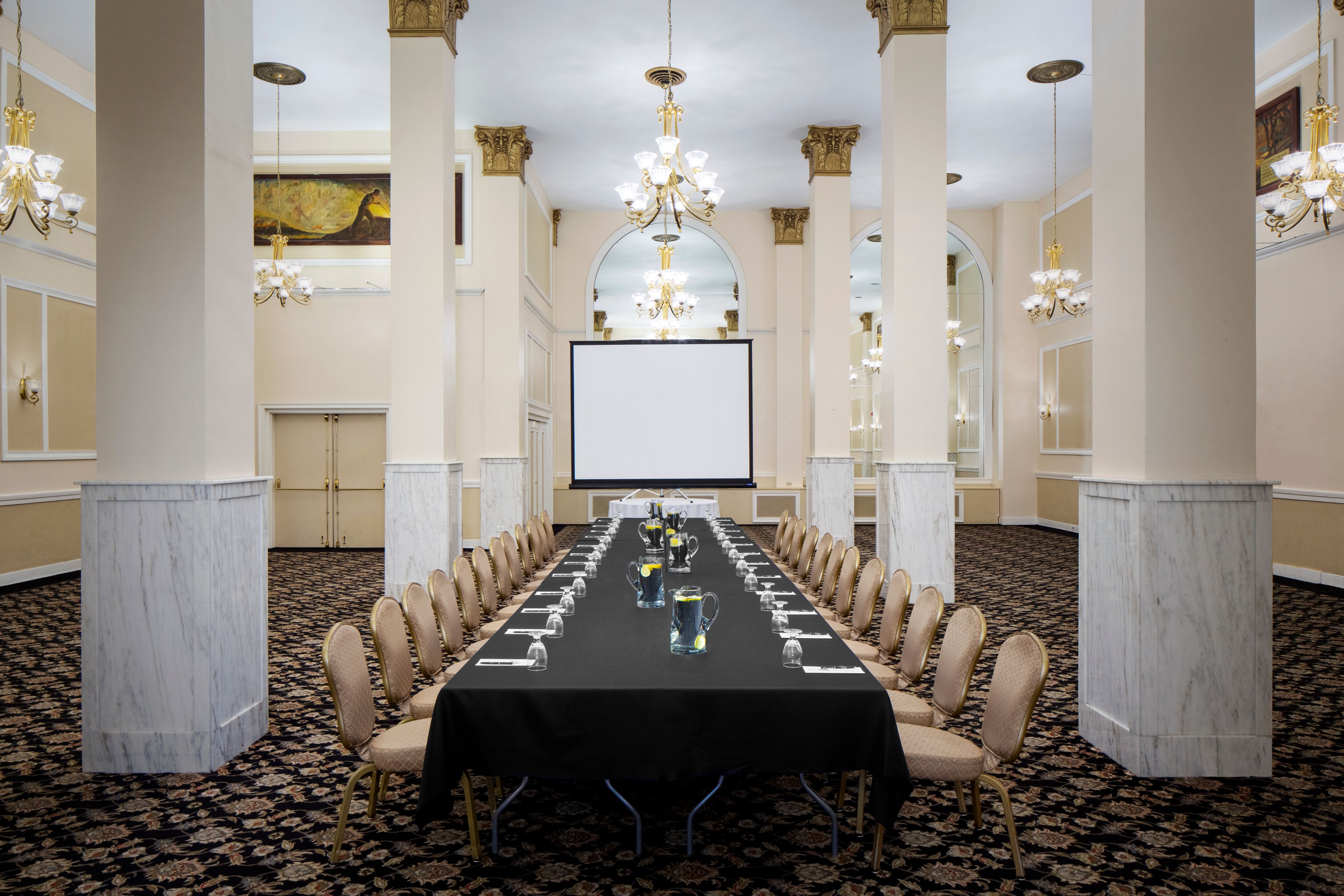 a long table with chairs in a room with columns and chandeliers