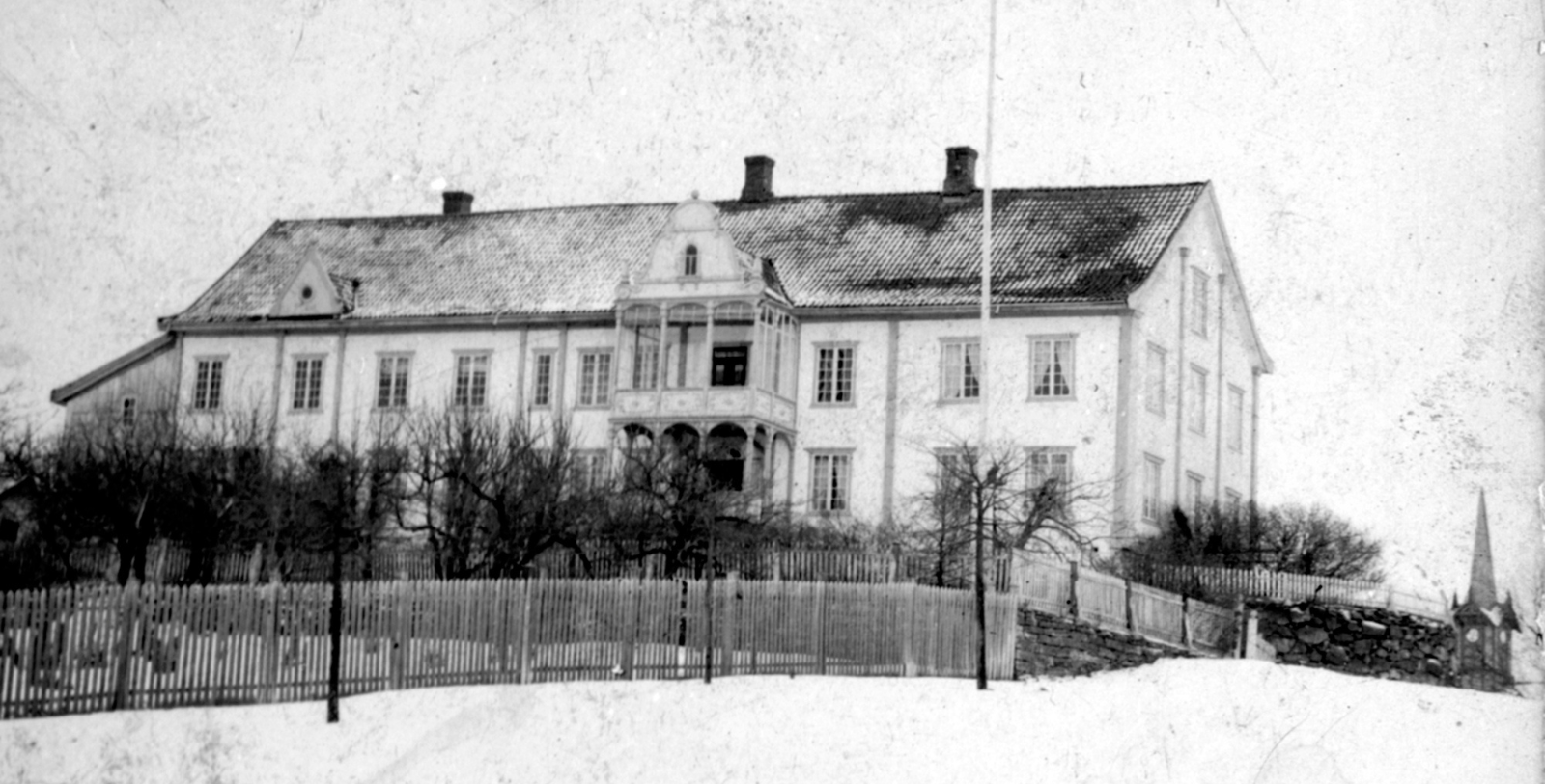 a large white house with a fence and trees in the snow