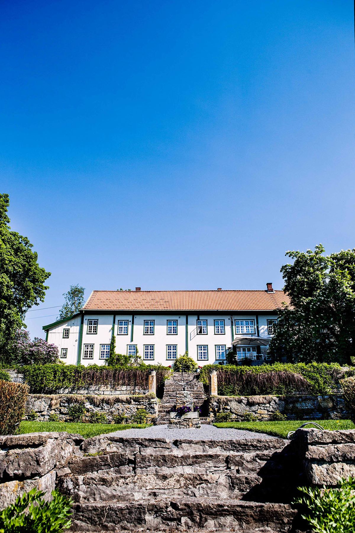a large white building with a stone wall and trees