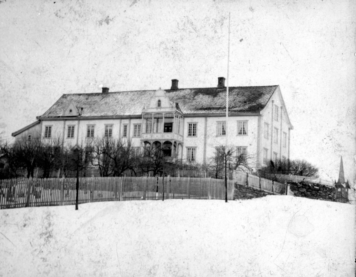 a large white house with a fence and trees in the snow