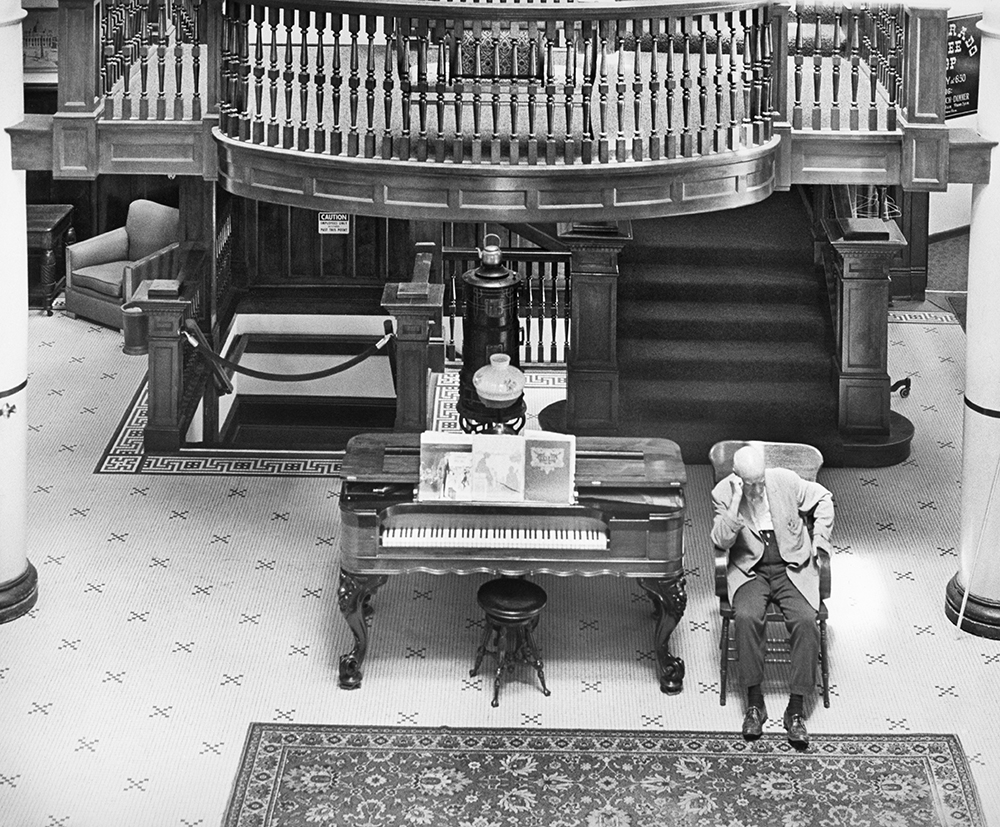 an old man sitting in a chair in front of a piano