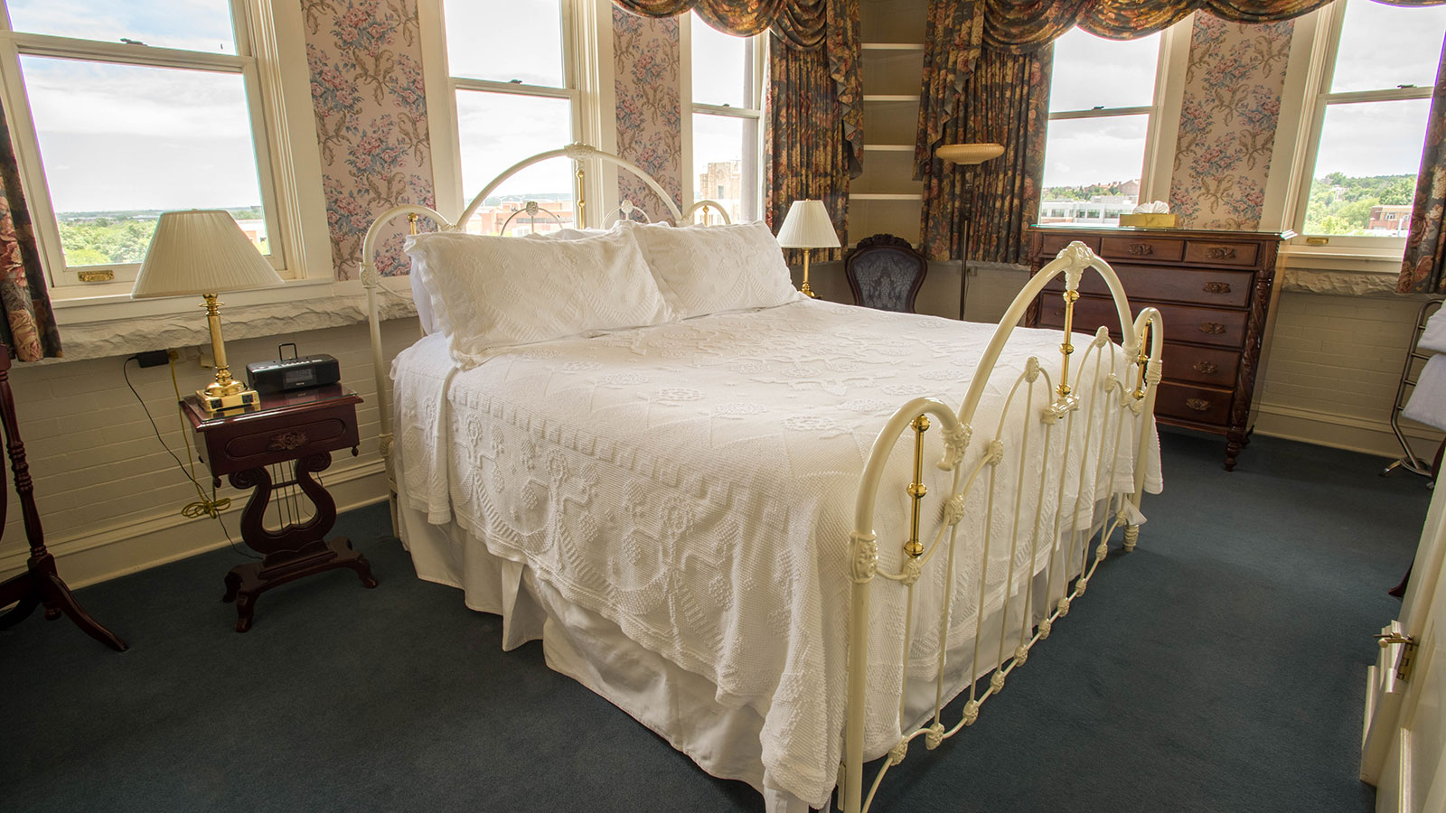 a bed with white sheets and pillows in a room with windows