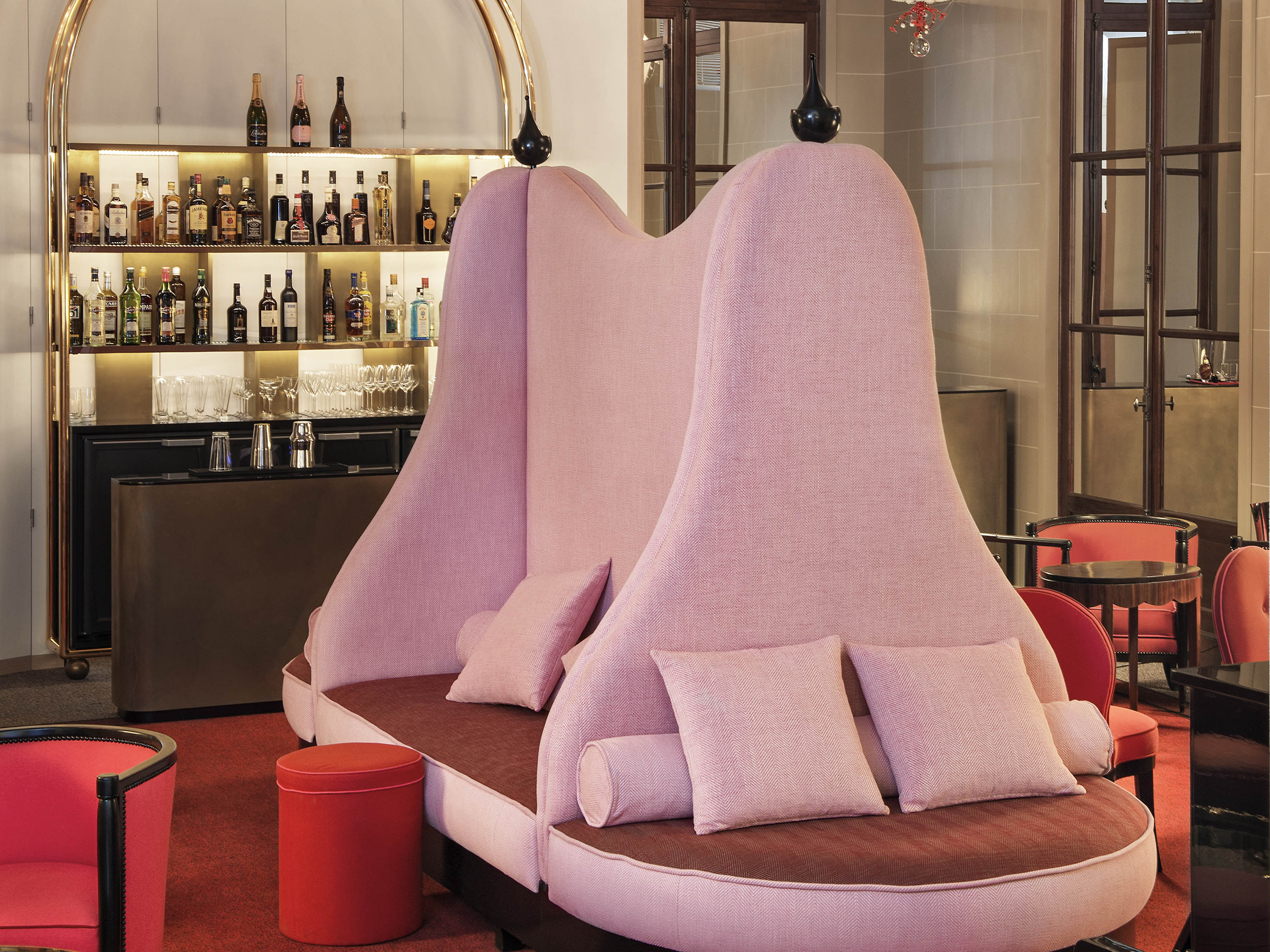 a pink couch with pillows in a room with shelves of liquor