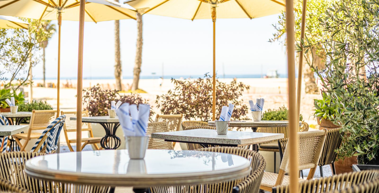 tables and chairs outside with umbrellas and a beach in the background