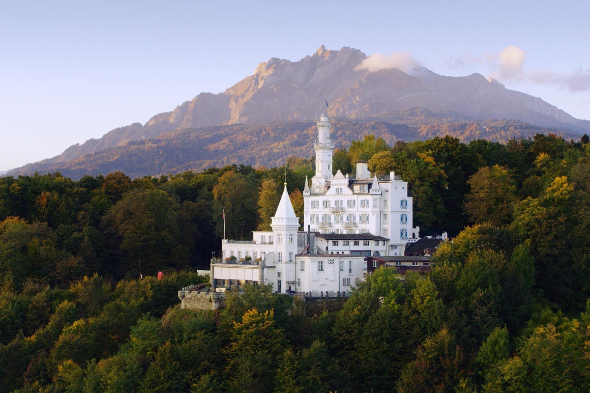 a white building with a tower and a tower on top of a hill with trees and mountains in the background