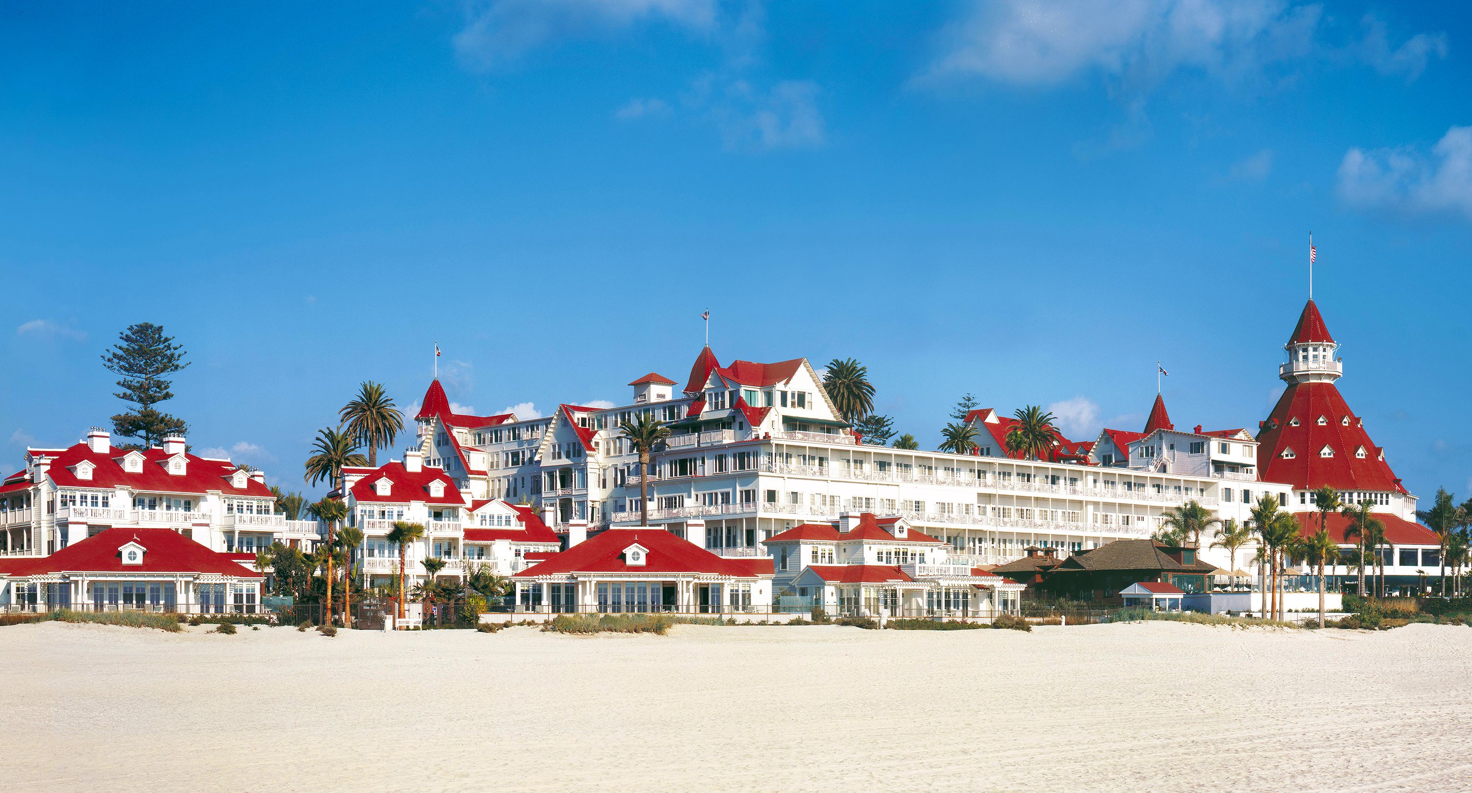 a large white building with red roofs and a beach with Hotel del Coronado in the background