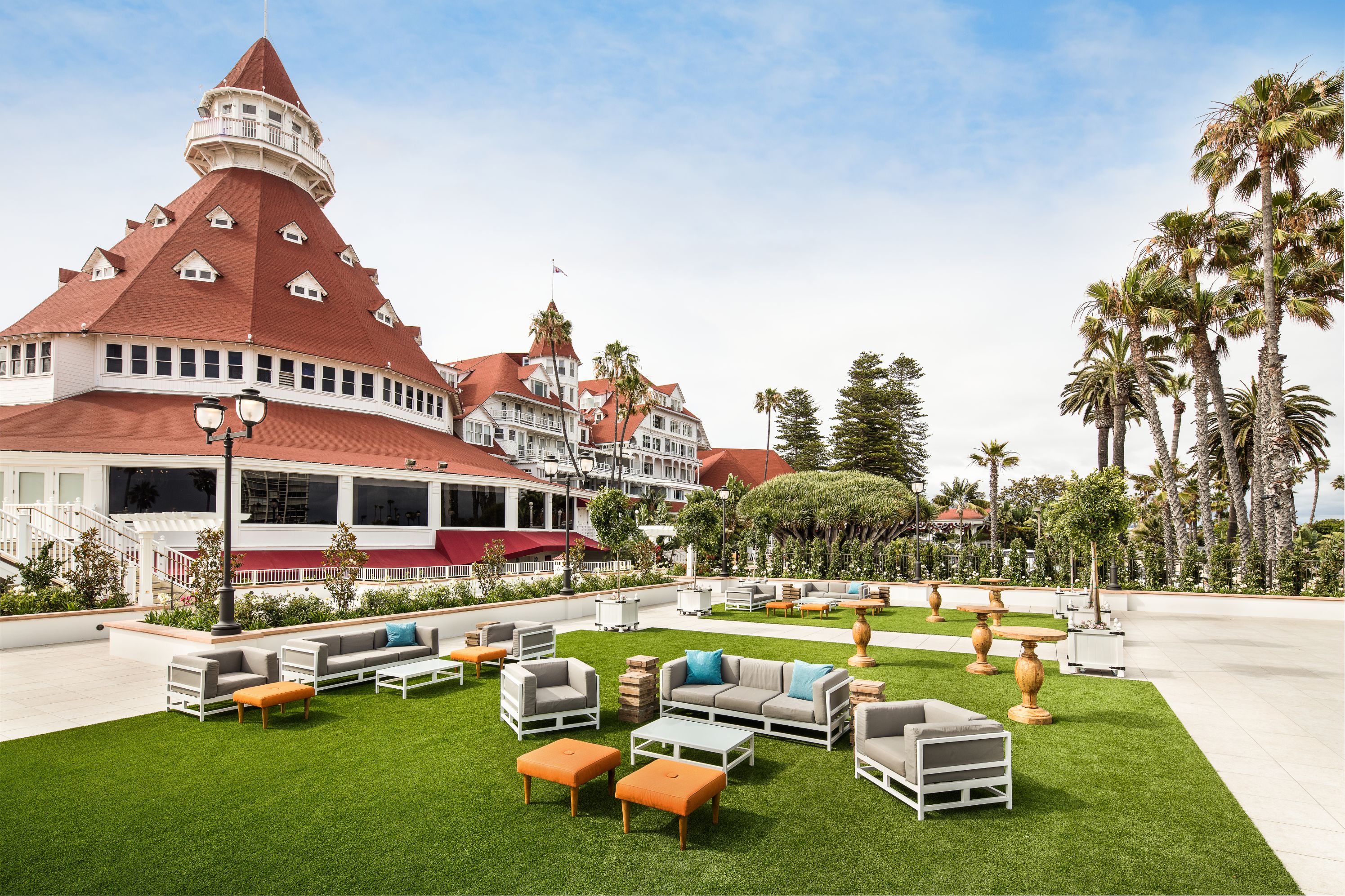 a large building with a large round structure and a lawn with chairs and tables with Hotel del Coronado in the background