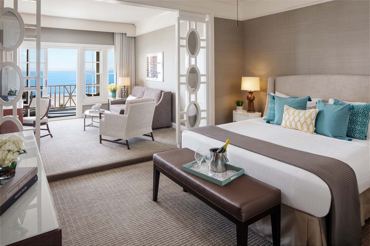 a room with a bed and chairs and a balcony overlooking the ocean