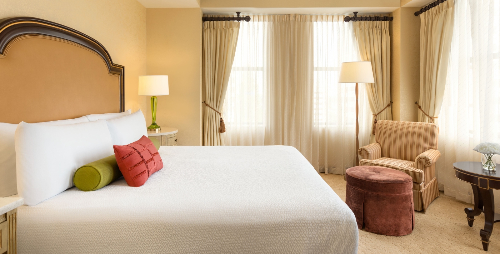 a bed with a red pillow and a chair in a room with curtains