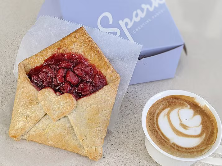 a pastry with a heart shaped filling next to a cup of coffee