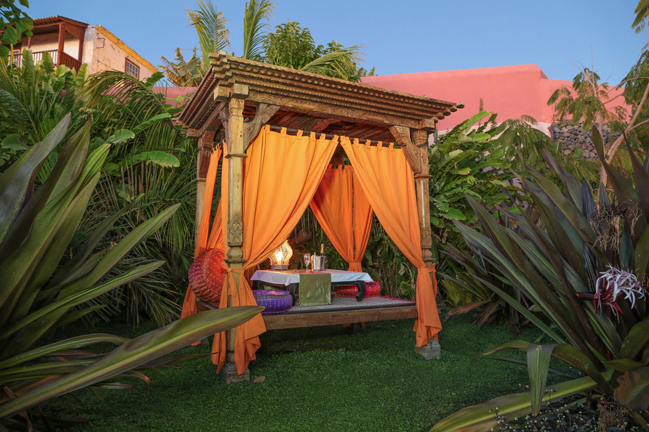 a wooden structure with orange curtains and a table in the middle of a yard