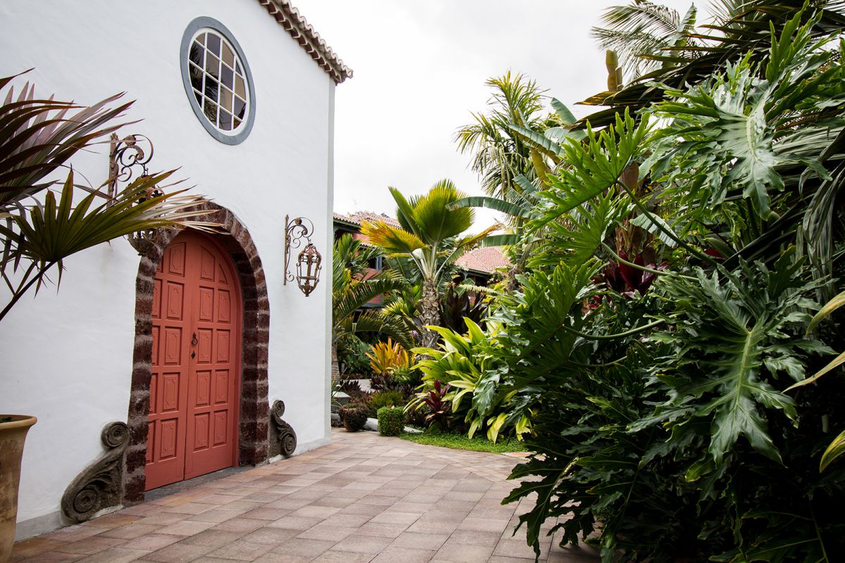 a white building with a red door and a red door surrounded by tropical plants