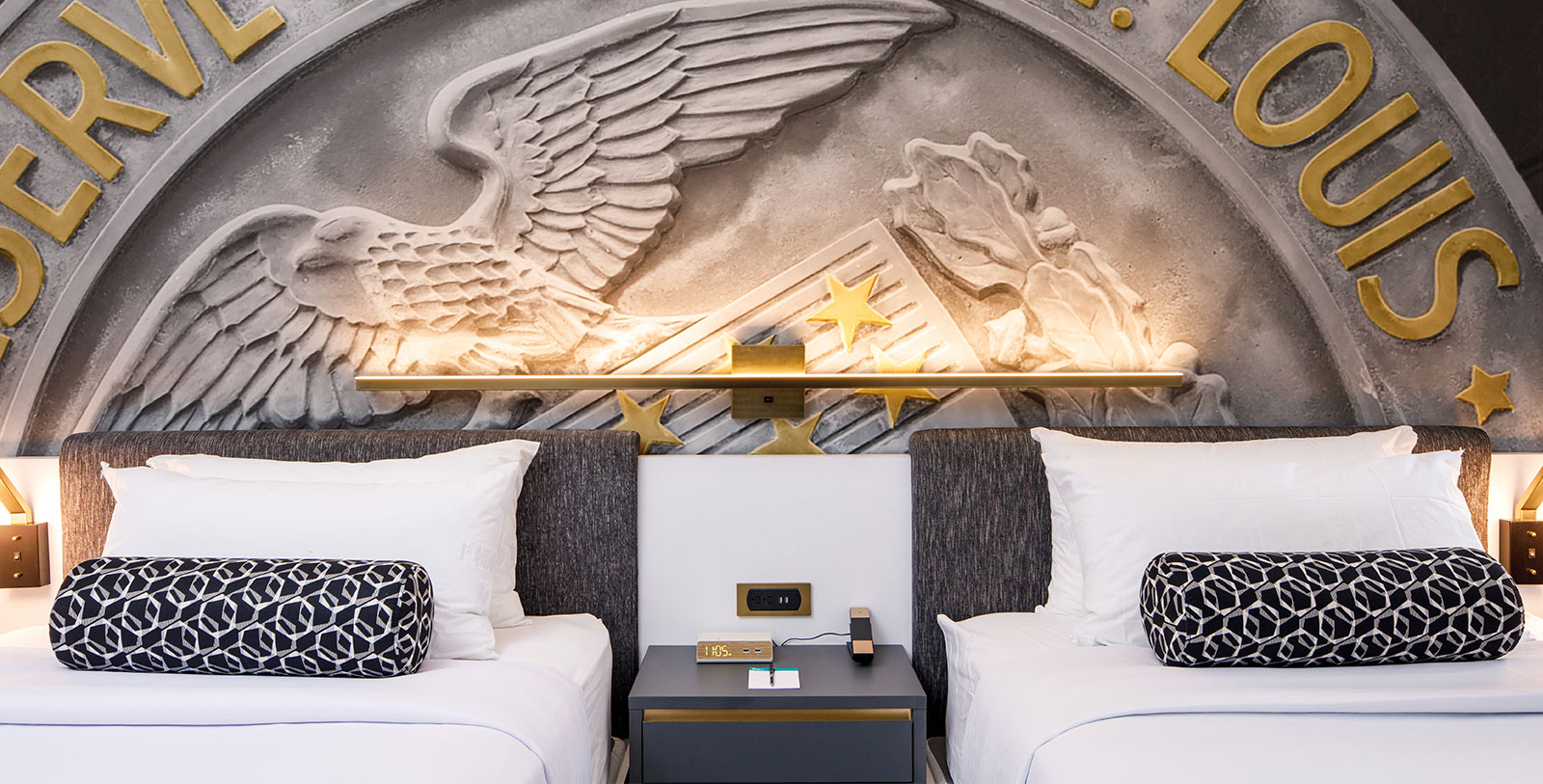two beds with pillows and a table in front of a wall with a sculpture