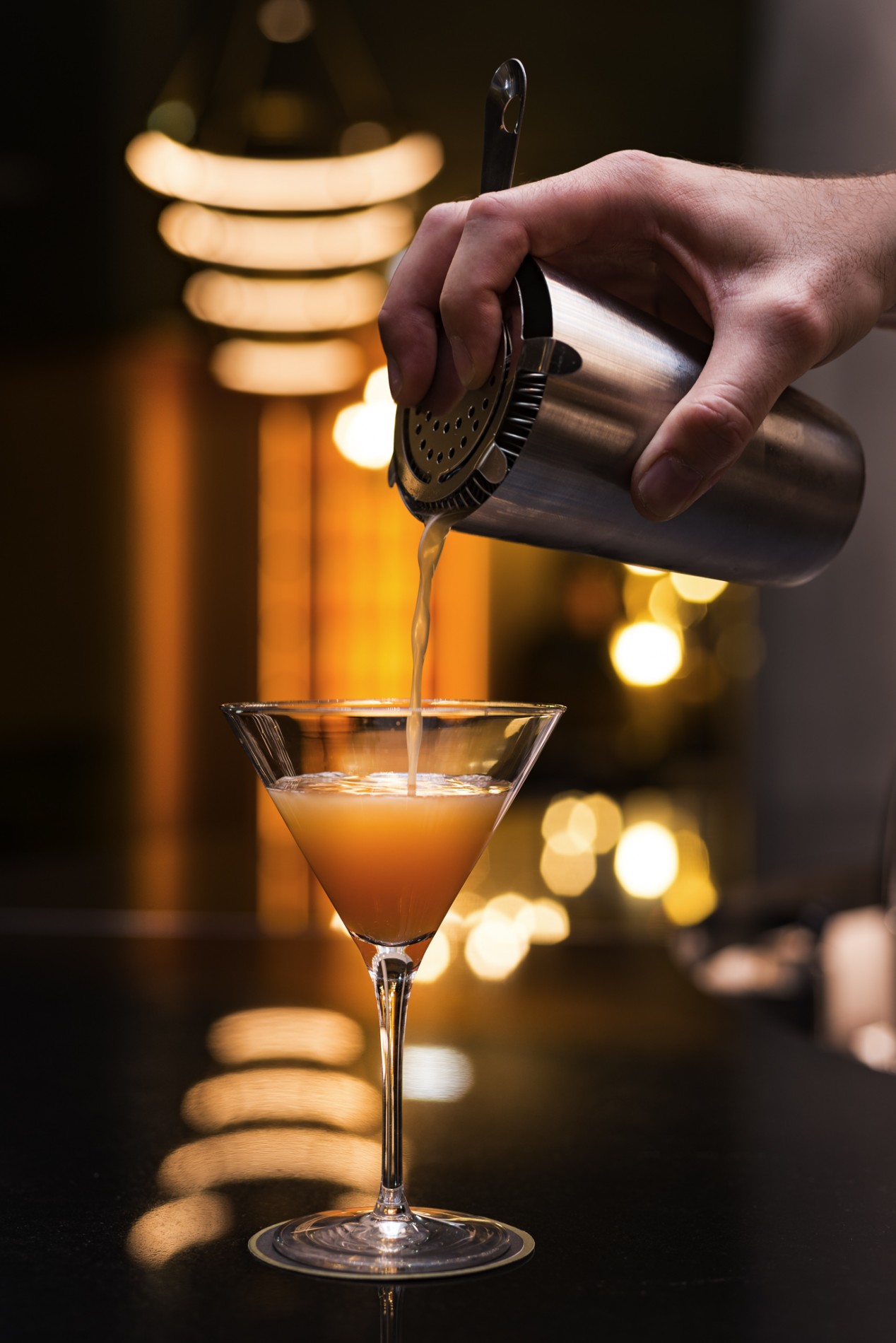 a person pouring a drink into a martini glass