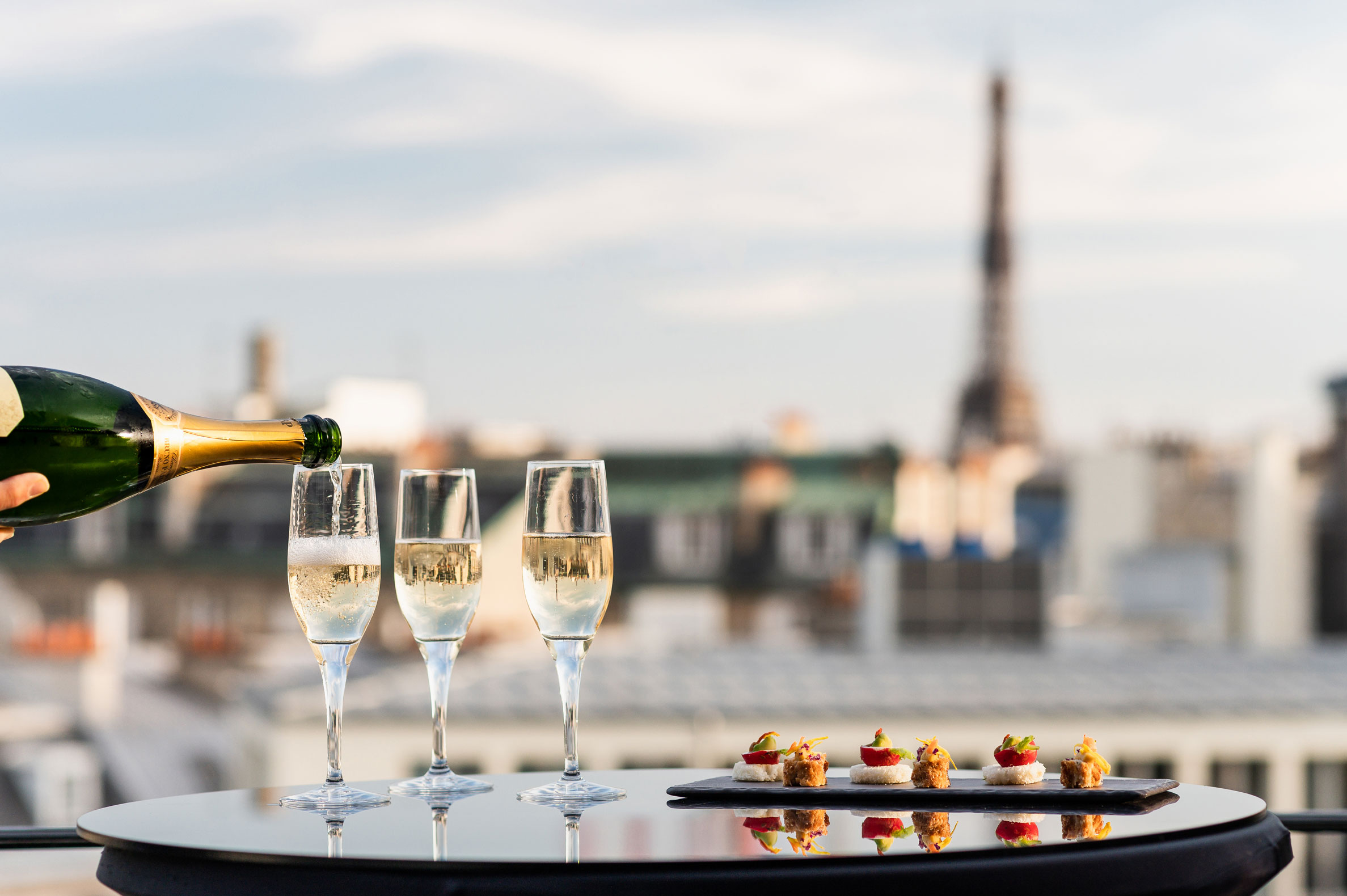 a person pouring champagne into glasses on a table with a city in the background