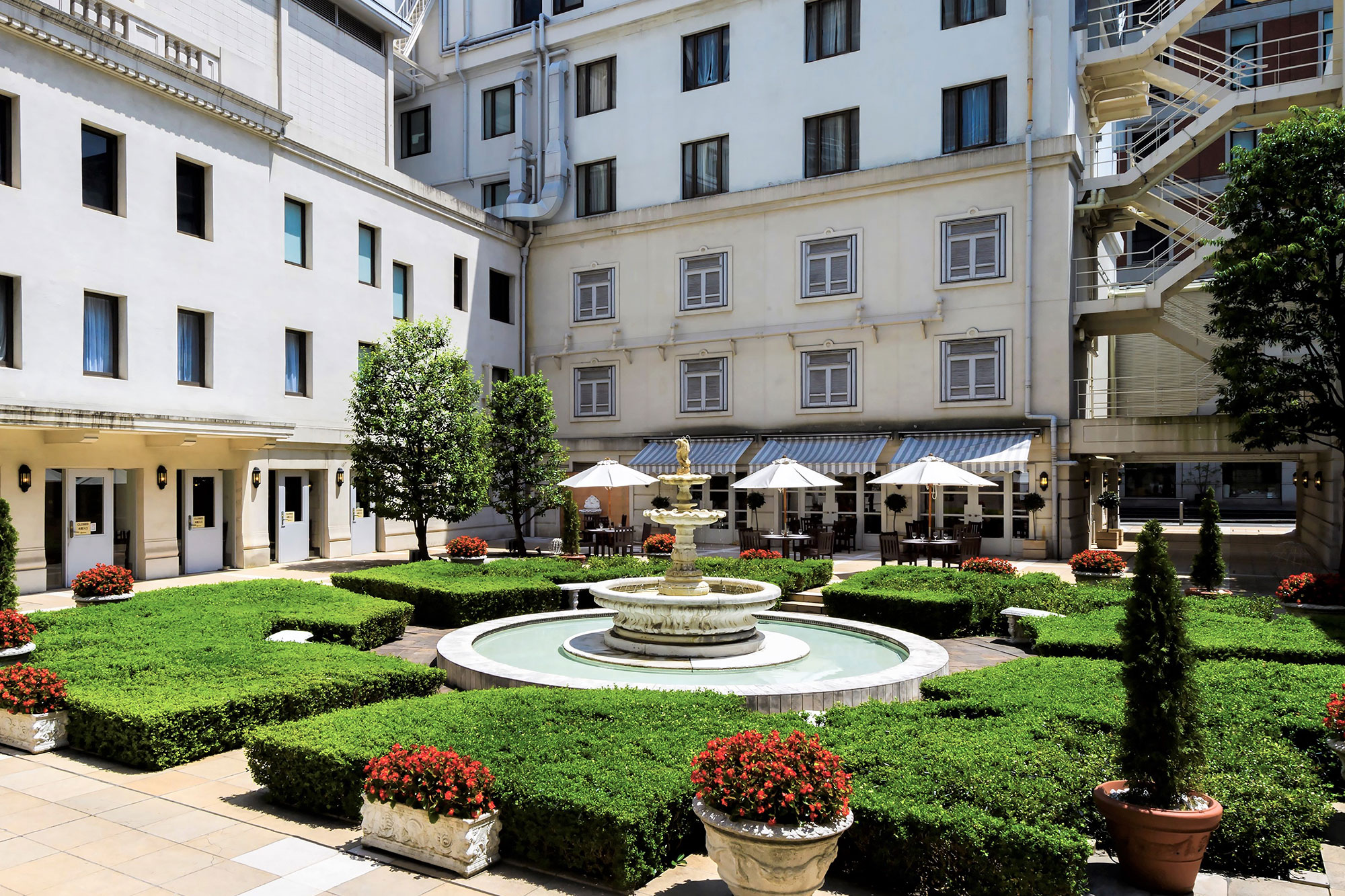 a fountain in a courtyard with bushes and umbrellas