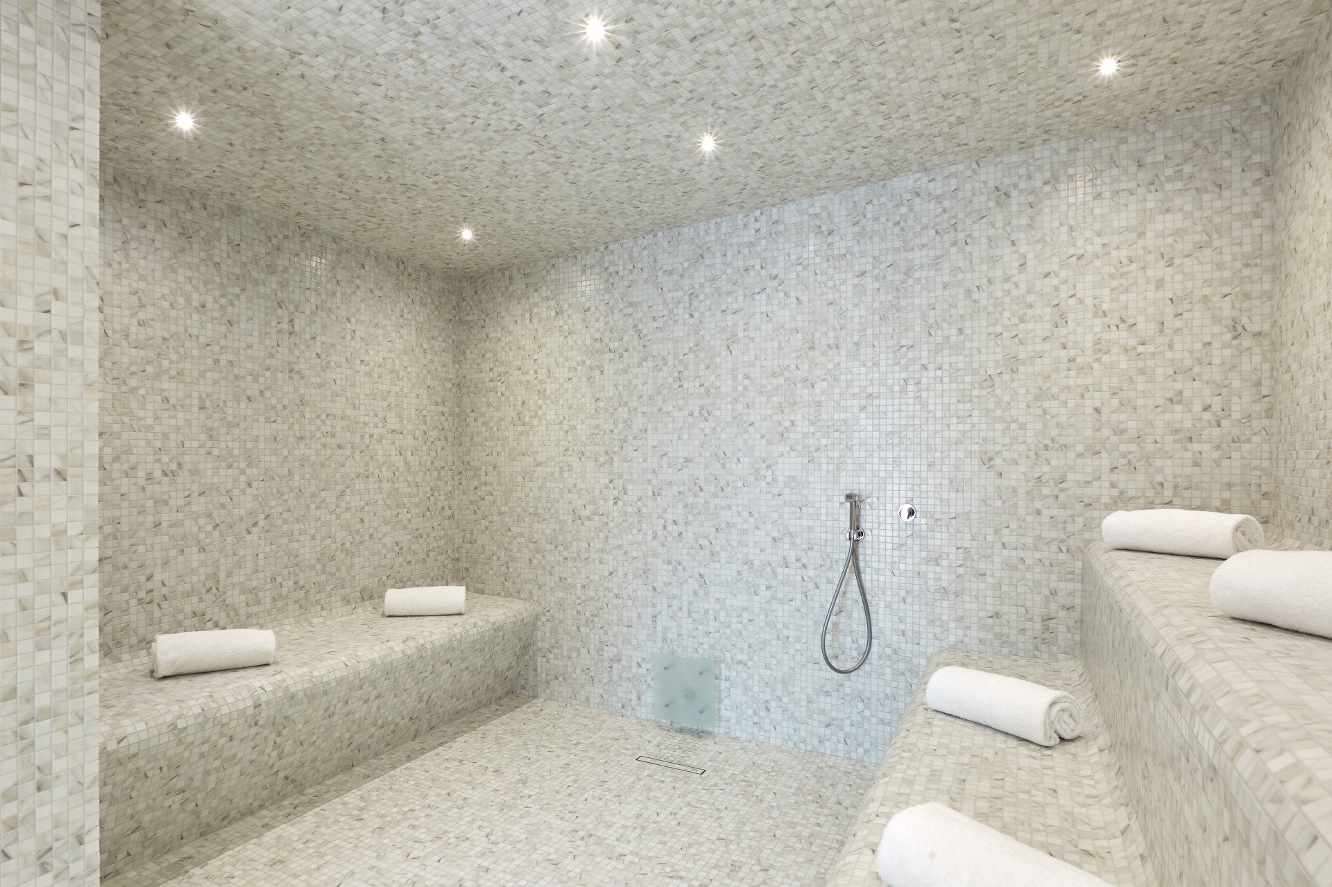a white tiled room with a shower and a bench