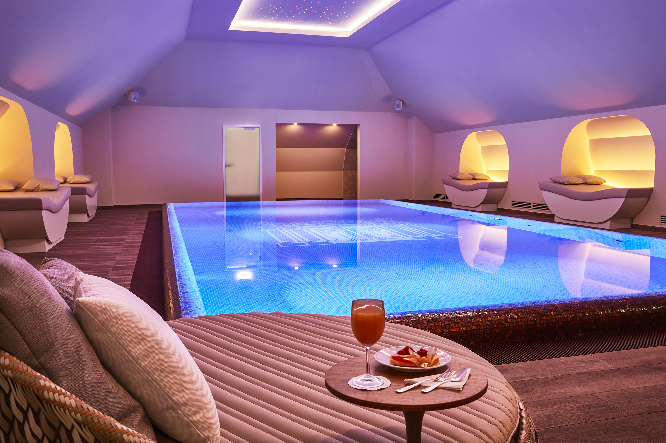 a pool with a glass of juice and a drink on a round table