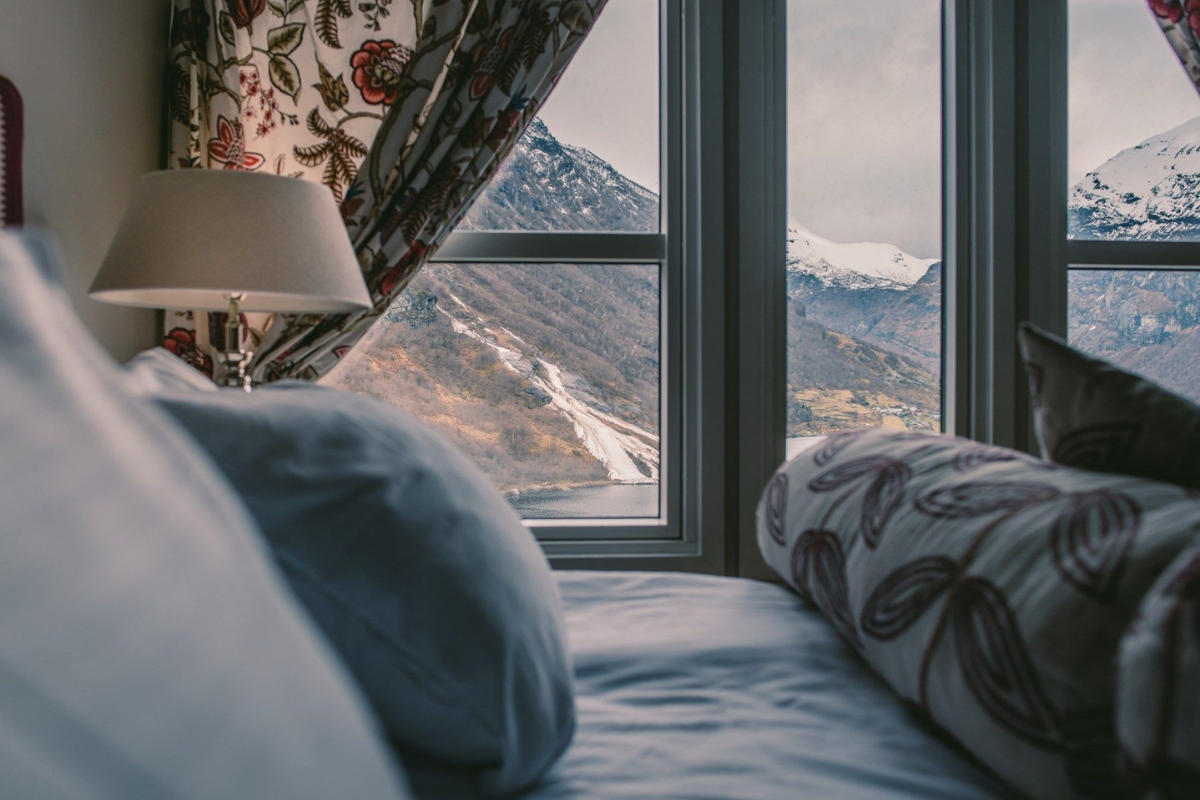 a window with curtains and a bed with a view of mountains