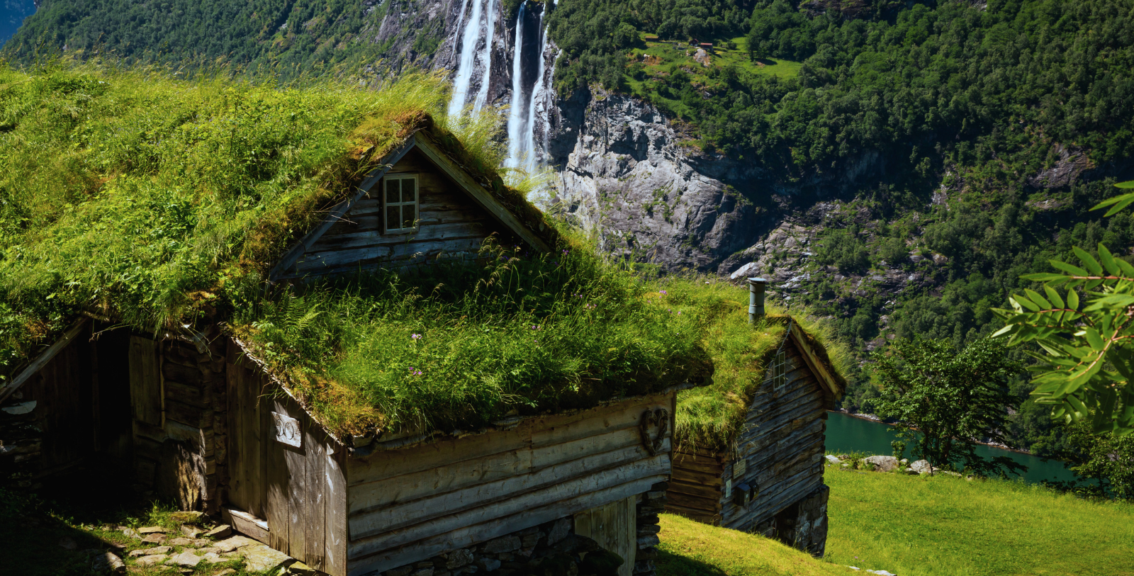 a two wooden buildings with grass on the roof and a waterfall in the background