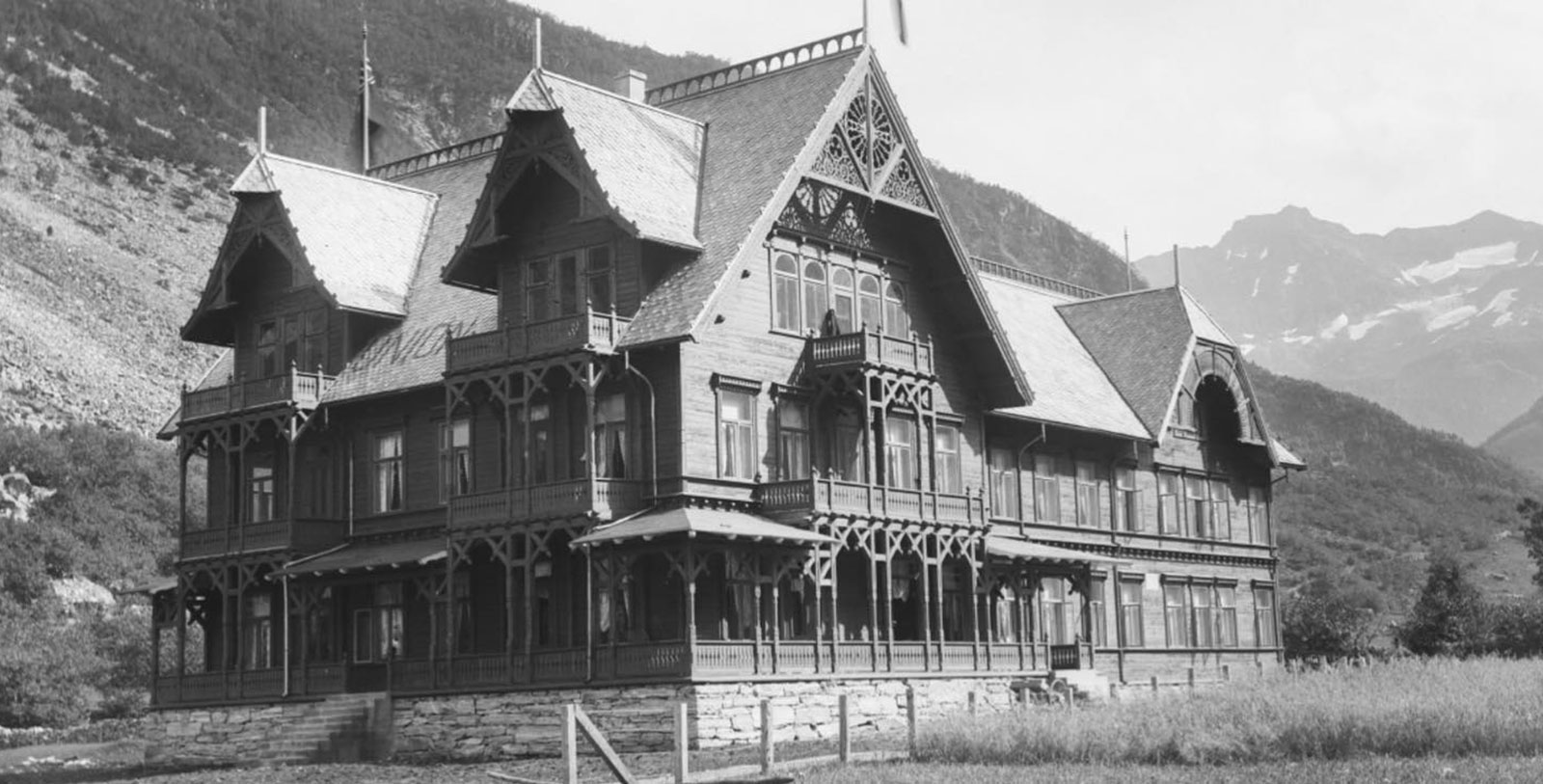 a large house with a fence and mountains in the background