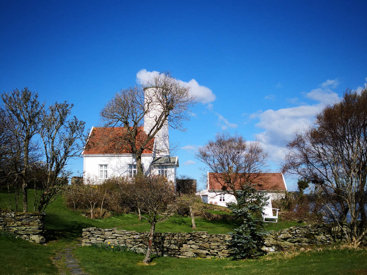 a white house with a chimney on a hill with trees and grass