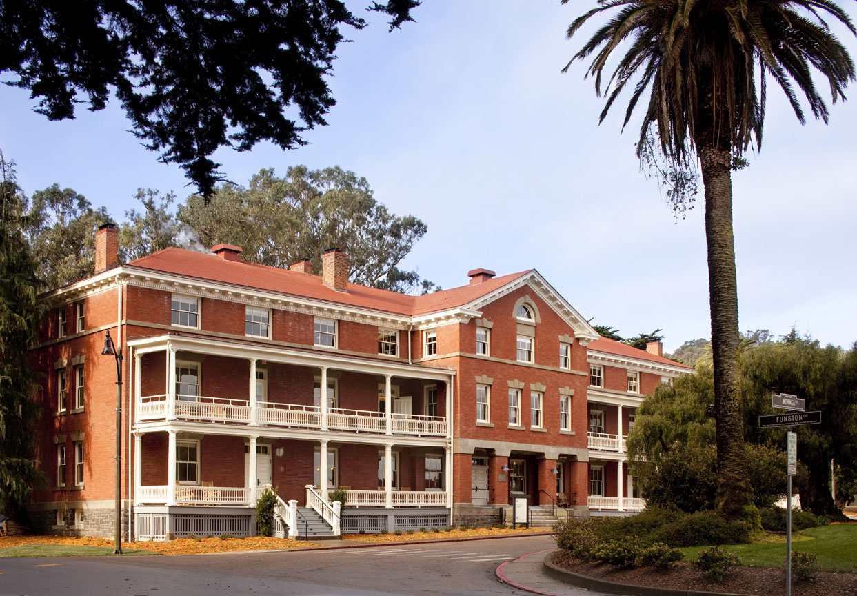 a large brick building with white trim with Presidio of San Francisco in the background