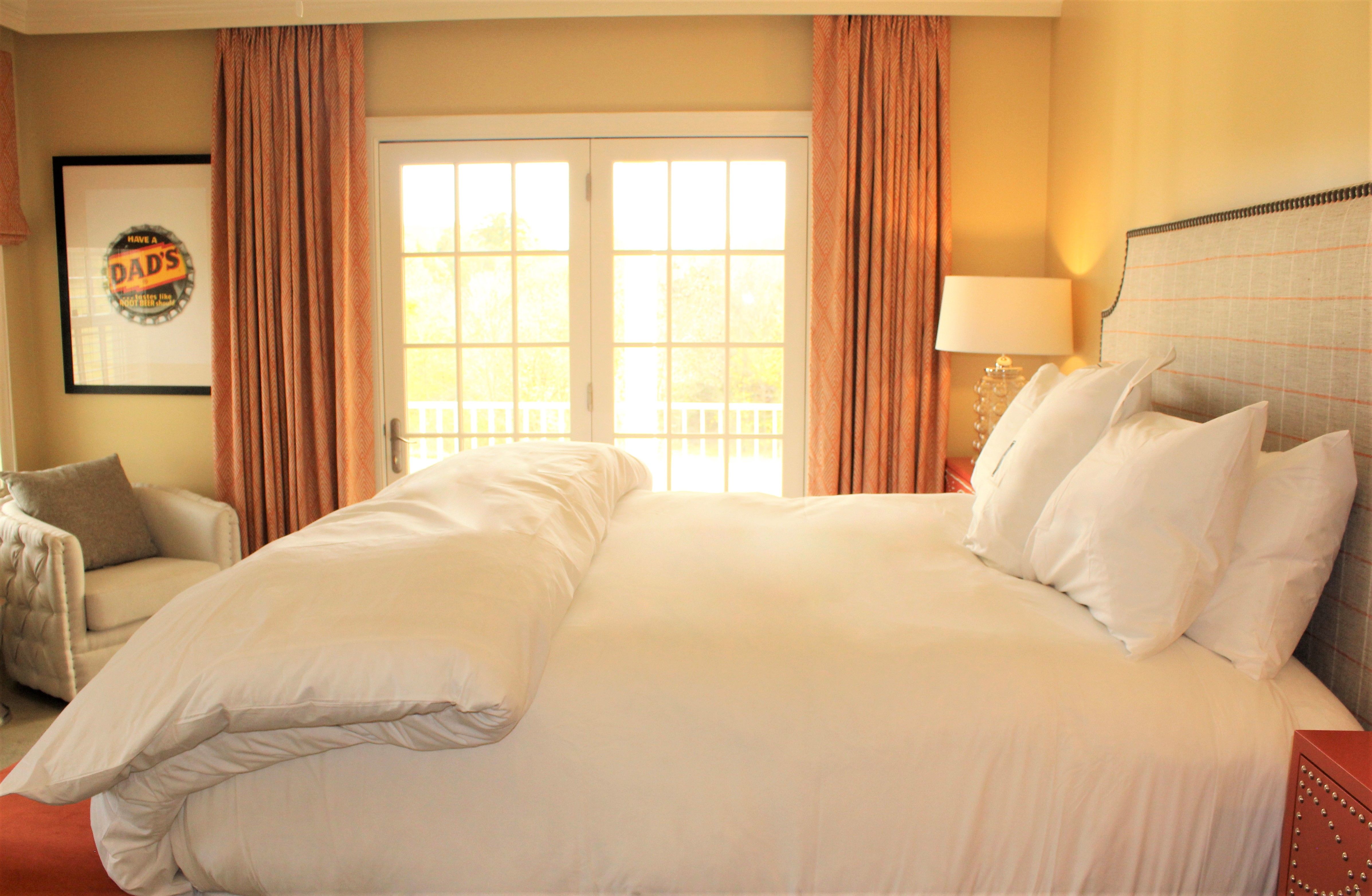 a bed with white sheets and pillows in a room with orange curtains
