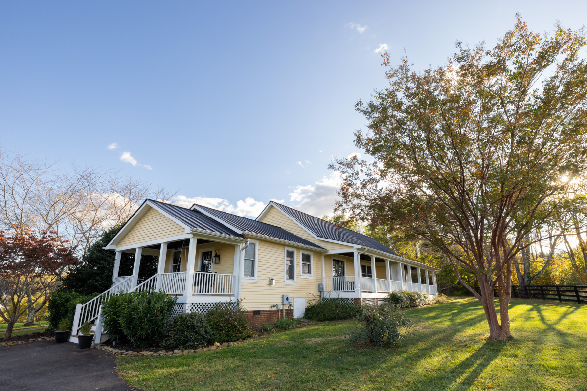 a yellow house with a porch and a tree