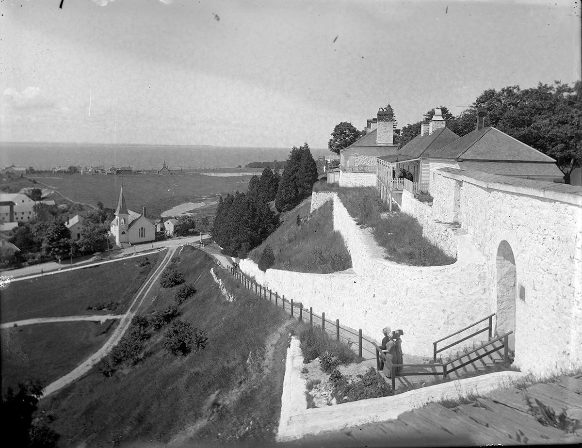 a black and white photo of a building with a hill and trees