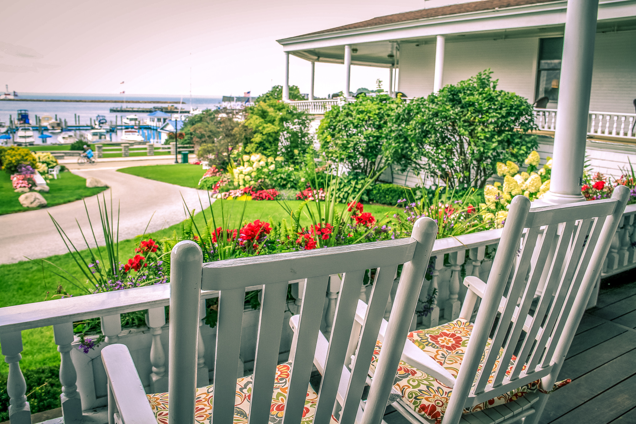 a white wooden chairs on a porch overlooking a yard with a house and water in the background